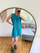 Vestido corto de algodón color turquesa, sin mangas y con cuello redondo. Presenta un tejido calado con diferentes patrones de punto.