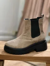Bota estilo Chelsea de cuero con textura granulada en tono beige. Presenta paneles elásticos laterales en color negro y una suela track de plataforma y taco cuadrado en color negro.