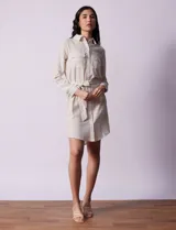 Vestido camisero corto a rayas verticales celestes y blancas, con cuello con solapa, abertura frontal con botones, dos bolsillos de parche en el pecho y lazo de ajuste en la cintura.