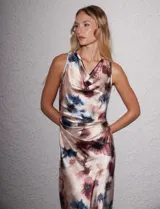 Vestido midi de satén fluido con estampado floral en tonos beige, azul y borravino. Presenta cuello volcado, diseño sin mangas y un drapeado lateral fruncido en la cintura que aporta movimiento a la falda de corte evasé.