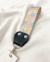 Llavero de tela estampada con diseño de fantasmas y detalles en cuero sintético negro. Incluye mosquetón metálico plateado.