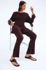 Pantalón de tiro alto, color marrón oscuro, confeccionado en tejido de punto acanalado. Presenta elástico oculto en la cintura y bajos acampanados con abertura lateral.