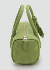 Bolso de mano cilíndrico de cuero gamuzado color verde, con dos asas cortas y detalle de lazo decorativo en un lateral. Cuenta con cierre superior de cremallera.
