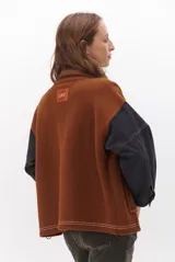 Campera color caramelo con mangas de denim azul oscuro. Presenta cuello alto, cierre frontal con botones, cuatro bolsillos delanteros con solapa y pespuntes blancos decorativos.