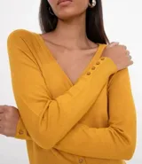 Cardigan de punto color mostaza con escote en V y cierre frontal de botones. Presenta mangas largas y diseño ajustado al cuerpo.
