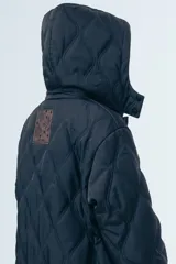 Campera acolchada de largo midi en color negro, con diseño de matelassé romboidal, cierre frontal con botones y capucha desmontable.