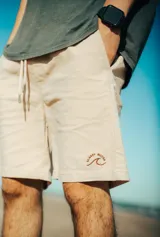 Bermuda color beige con cordón ajustable en la cintura y logo bordado en la pierna derecha.