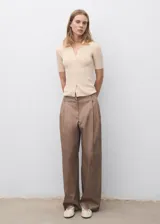 Jersey de punto fino color beige, con cuello camisero, manga corta y cierre frontal con botones pequeños. Diseño entallado de canalé.