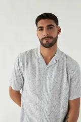 Camisa de manga corta con cuello cubano, confeccionada en viscosa con estampado de hojas en tonos azules. Presenta cierre frontal abotonado y corte slim.