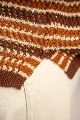 Sweater de punto con diseño de rayas horizontales en tonos ocre, marrón y crudo. Presenta cuello redondo, mangas largas y puños acanalados.
