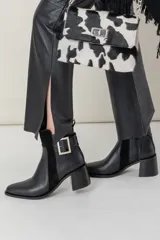 Botas de cuero negras con detalles de gamuza en los laterales y una hebilla plateada decorativa en el tobillo. Tienen punta cuadrada y tacón ancho.