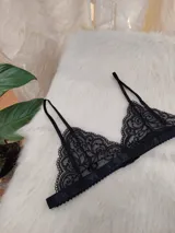 Bralette triangular de encaje negro con diseño floral, breteles finos regulables y banda elástica inferior.