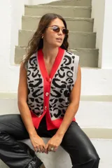 Chaleco tejido de punto con estampado animal print en tonos gris y negro, con borde frontal y ruedo en color rojo vibrante. Presenta cierre frontal con botones y un diseño holgado.