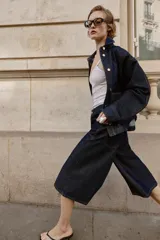 Bermuda de tiro alto confeccionada en denim azul oscuro, con diseño de pernera ancha, cinco bolsillos y cierre frontal con cremallera y botón.