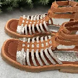 Sandalias bajas de cuero color beige con tiras horizontales plateadas y cierre con hebilla al tobillo.