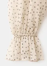 Blusa de gasa color beige con estampado de lunares negros, cuello alto con lazo integrado y mangas largas con puños amplios.