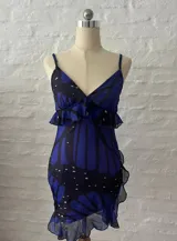 Vestido corto de microtul con estampado de mariposas azules y negras sobre fondo negro. Tiene breteles finos, escote en V con volados y falda con volados y abertura lateral.
