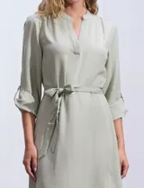 Vestido maxi color beige, con cuello mao y escote en V. Presenta mangas largas con presilla y botón para regular el largo, y un lazo ajustable en la cintura que marca la silueta.