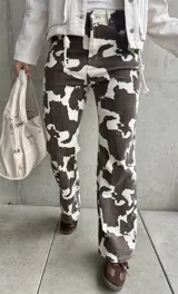 Pantalón de jean de corte recto con estampado de manchas de vaca en tonos marrón y blanco.