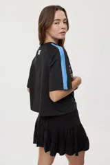 Remera blanca de manga corta, con cuello redondo, calce relajado y estampado frontal con motivos gráficos de soles y símbolos marinos en tonos rosados y bordo, además de líneas horizontales.