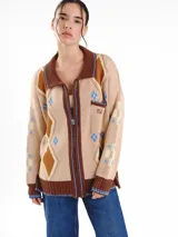 Campera tejida en jacquard con diseño geométrico de rombos, cuello tipo polo, cierre frontal completo y un bolsillo en el pecho. Presenta terminaciones en marrón contrastante con detalles bordados a mano.