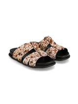 Sandalias planas con tiras cruzadas de pelo con estampado animal print tipo vaca en tonos blancos y marrones, con suela negra.
