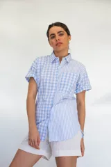 Camisa de manga corta con combinación de patrones a rayas y cuadros en tonos celeste y blanco, con bolsillo frontal aplicado y cierre de botones.