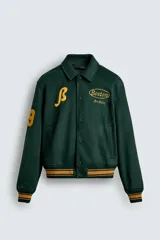 Cazadora tipo varsity de corte relajado confeccionada en tejido efecto ante color verde oscuro. Presenta cuello solapa, cierre frontal con botones a presión y puños y bajo acanalados con rayas en contraste. Incluye parches bordados en color amarillo en el frente y mangas.