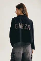 Buzo negro de algodón, con cuello polo y cierre frontal de botones, manga larga y calce oversized cropped. Presenta pequeño estampado tono sobre tono en el ruedo.