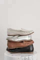 Mocasines de cuero color dorado con acabado texturizado, diseño clásico de punta redondeada y costuras visibles en el empeine. Cuentan con suela plana y flexible.