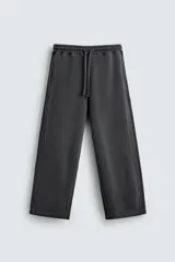 Pantalón jogger de corte wide fit confeccionado en tejido de algodón con interior de rizo. Presenta cintura elástica ajustable con cordón, bandas laterales decorativas, bolsillos laterales y un bolsillo trasero de plastrón. El acabado presenta un efecto lavado que le otorga una apariencia única.