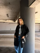 Camisa larga negra con cuello clásico, cierre frontal con botones a presión, mangas largas con puños de cuero y bolsillos de cuero con pespuntes blancos.