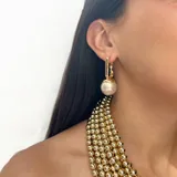 Aros tipo argolla rectangular de acero dorado con perla colgante engarzada. Diseño liviano e hipoalergénico con cierre de perno para perforación.