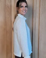 Camisa de manga larga con estampado de rayas verticales en tonos crudo y beige. Presenta cuello alto con volados, cierre frontal con botones dobles y puños con volados.