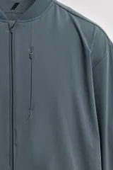 Chaqueta técnica de corte relajado, confeccionada en tejido compacto y elástico. Presenta cuello y puños acabados en rib, cierre frontal con cremallera, bolsillos frontales con cremallera oculta y bajo ajustable con elástico en los laterales.