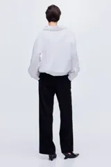 Pantalón ancho negro de corte holgado con pinzas, cierre frontal oculto y pliegues marcados en las piernas.