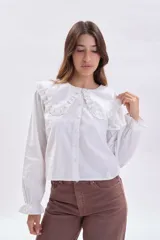 Camisa blanca de manga larga con cuello grande estilo babero con detalles de bordado inglés (broderie), cierre frontal con botones y puños elásticos con volados.