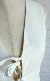 Chaleco blanco sin mangas, con escote en V profundo y cierre frontal mediante lazos anudados.