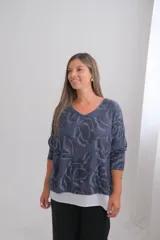 Sweter de punto con diseño de flores estampadas en tonos azules, con cuello en V y mangas tres cuartos. Presenta un diseño de doble capa con un borde inferior en color blanco que sobresale.
