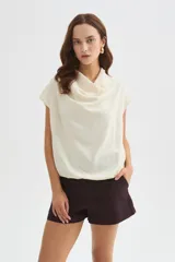 Blusa de poliéster color marfil, de corte holgado, sin mangas y con cuello buche drapeado.