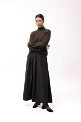 Polera de tejido de punto color marrón, con cuello alto y diseño de trenzas verticales. Presenta mangas largas con puños ajustados y un detalle de panel lateral asimétrico que se anuda en la cintura.