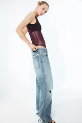 Body sin mangas de cuello redondo, confeccionado en una combinación de tul transparente y paneles de tela opaca a tono. Presenta un diseño ajustado con cierre inferior mediante botones a presión.