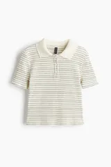 Remera polo de punto acanalado, color crema con finas rayas horizontales negras. Es de manga corta, corte entallado y cuello clásico con tapeta de botones.