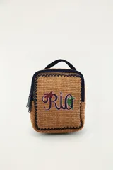 Bolso tote de mano color tostado, tejido con textura tipo mimbre o rafia, con bordes y detalles en azul marino. Cuenta con un asa superior corta, cierre con cremallera y un bordado frontal con la palabra "Rio" que incluye motivos tropicales de una palmera y un tucán.