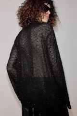 Camisa de hilatura con viscosa color negro, con cuello subido y manga larga ancha. Presenta aplicaciones de abalorios combinados a tono en toda la prenda y bajo recto.