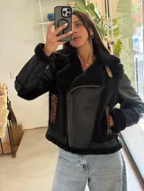 Campera tipo gamulán de cuero genuino en color negro, con interior y detalles de cuello en piel sintética negra. Presenta detalles en estampado animal print de leopardo en los bolsillos laterales y en la solapa. Cuenta con cierre frontal metálico y diseño de corte ajustado.