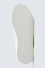 Zapatilla deportiva de cuero sintético color blanco, con suela de plataforma gruesa y detalle de gamuza gris en el talón.