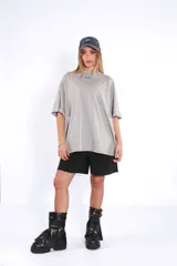 Remera oversize de algodón color gris claro, con cuello redondo y manga corta. Presenta un pequeño logo bordado en azul en el pecho.