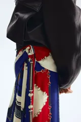 Pollera larga con diseño cruzado efecto pañuelo y brillo sutil. Presenta un estampado geométrico multicolor en tonos azul, rojo y crudo con detalles de cadenas.