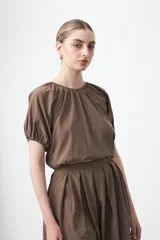 Top negro de manga corta con cuello redondo y frunces en el escote. El calce es holgado y se ajusta a la cintura con un elástico o banda ancha.